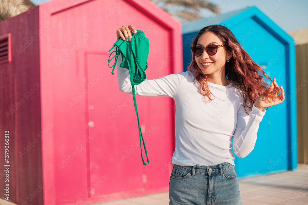 Tourist is getting ready for the beach, with a green swimsuit top in front of colorful changing rooms huts