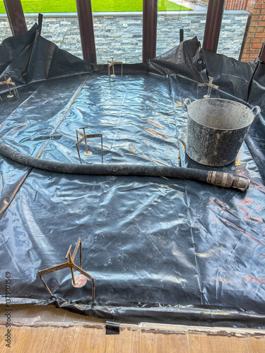 Plastic membrane , levelling equipment and hose on the floor of a new conservatory ready for concrete screed to be pumped into the area. No people.