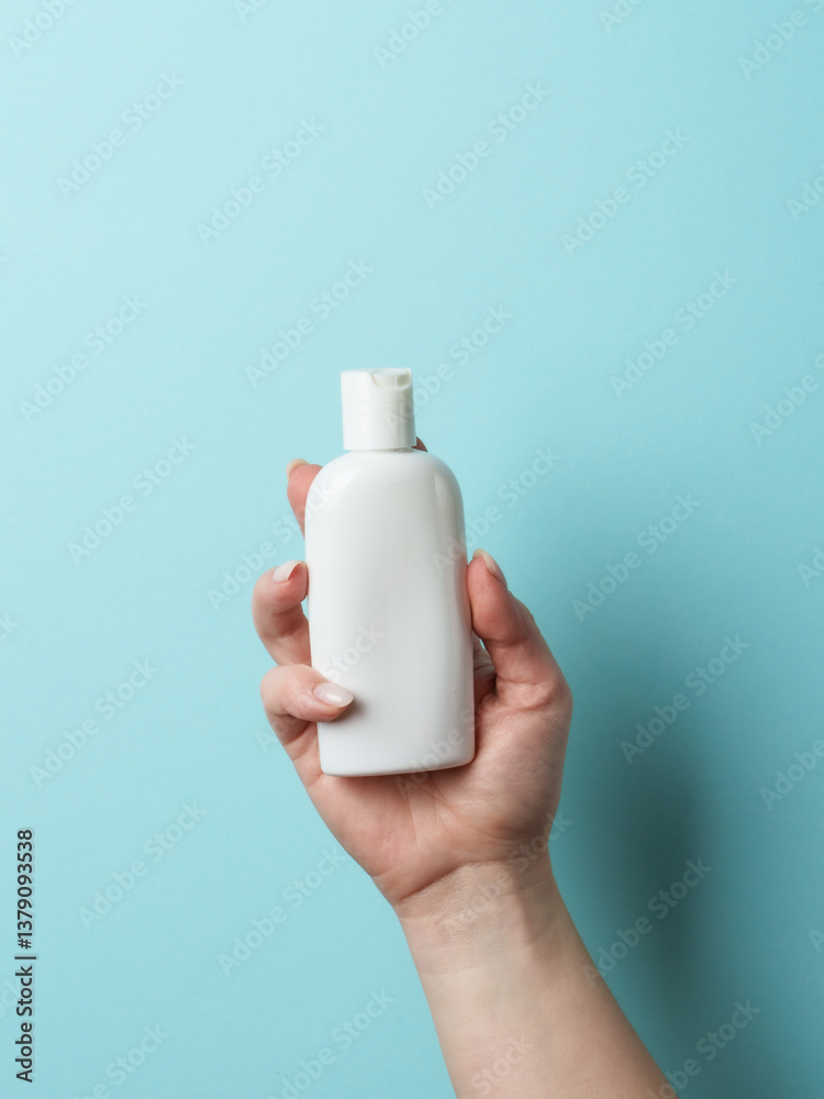Cosmetic bottle in woman hand on blue background.