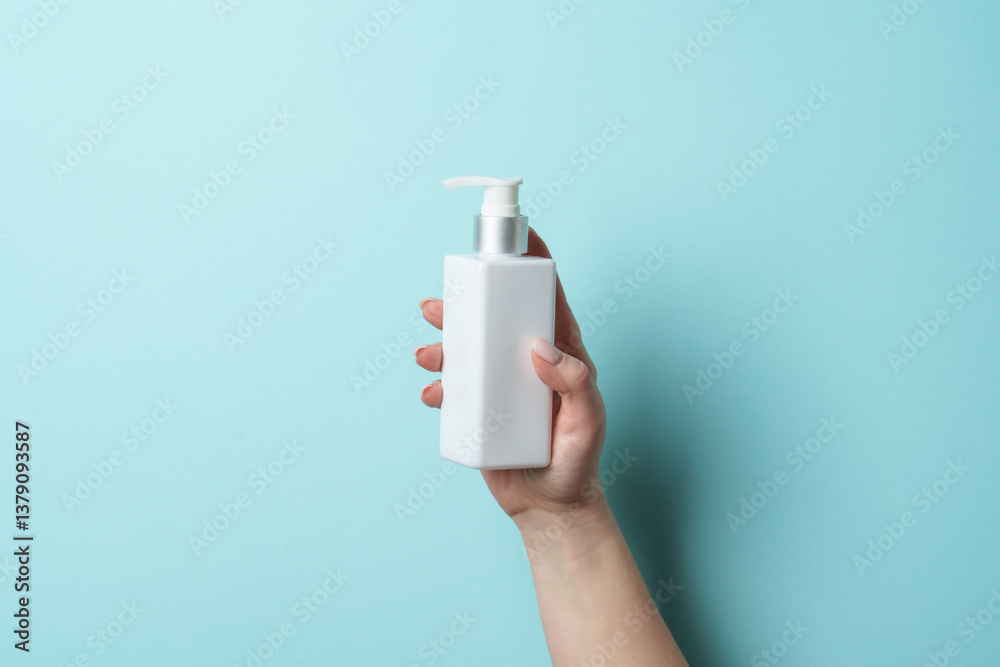 Cosmetic bottle in woman hand on blue background.