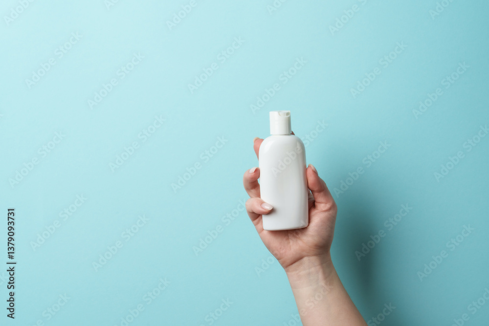 Cosmetic bottle in woman hand on blue background.