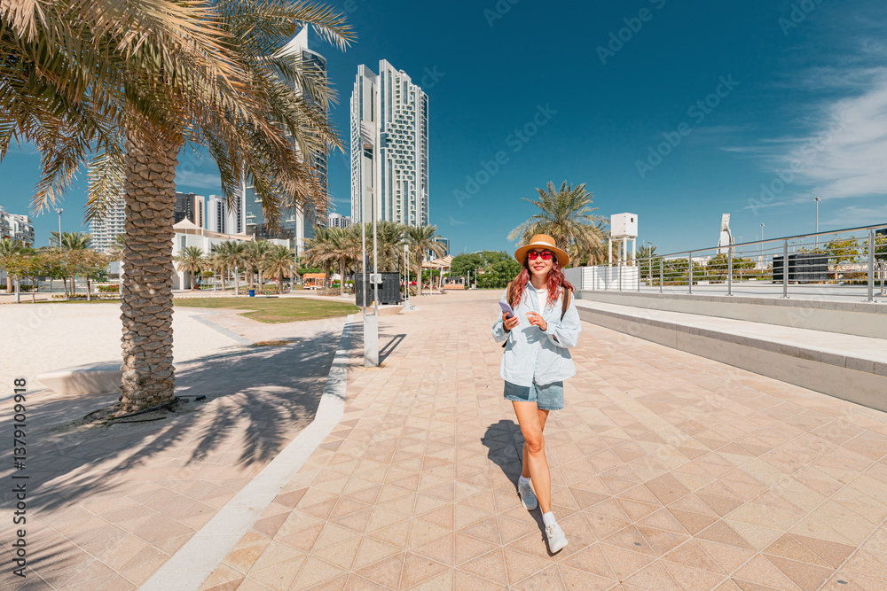 Young woman tourist walking in Abu Dhabi Al Reem park, using smartphone app and enjoying holidays in United Arab Emirates