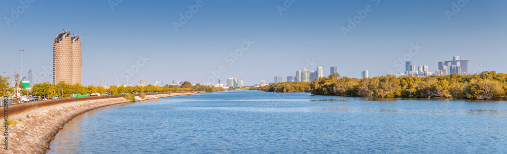Panoramic view of mangrove park with Abu Dhabi skyline in the background, featuring a promenade, lush vegetation and blue water
