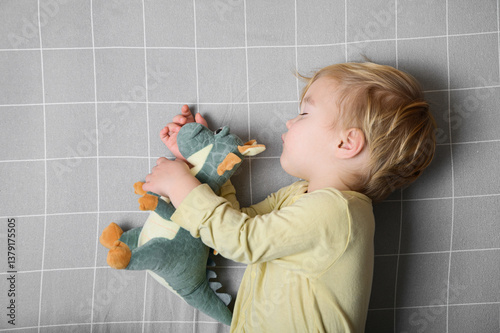 Sleeping Toddler Hugging Plush Dinosaur on Grey Grid Bed