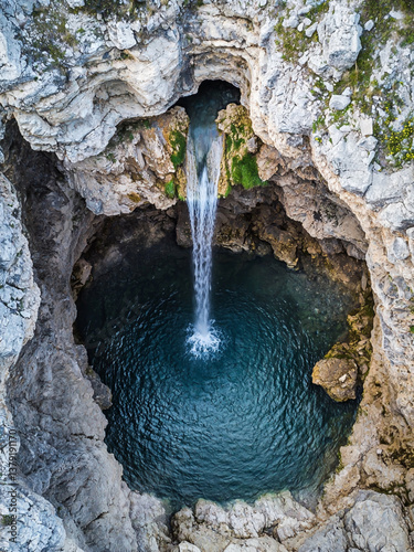 Aerial drone view of a waterfall flowing into a hidden grotto