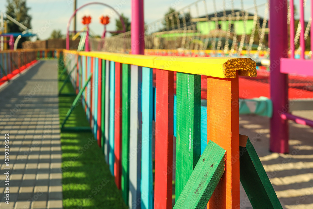 Colorful wooden fence with vertical planks in a children’s playground. Brightly painted in rainbow colors, shot in sunny weather with long shadows Colorful wooden fence with vertical planks in a children’s playground. Brightly painted in rainbow colors, shot in sunny weather with long shadows