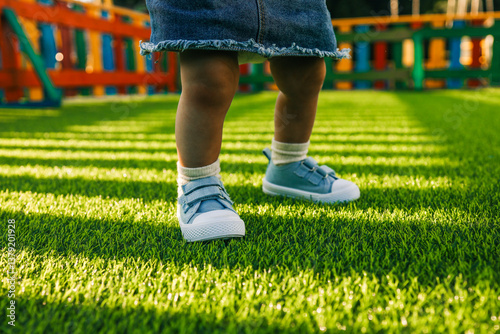 Wallpaper Mural Toddler in blue sneakers standing on bright green artificial grass in a colorful playground. Low angle view of children's legs on a sunny day Torontodigital.ca