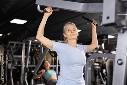 Mature female athlete working out at shoulder press machine in gym