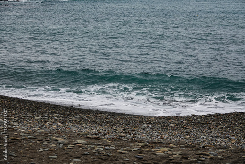 Waves softly crash onto a pebbled beach while the cloudy sky looms above.