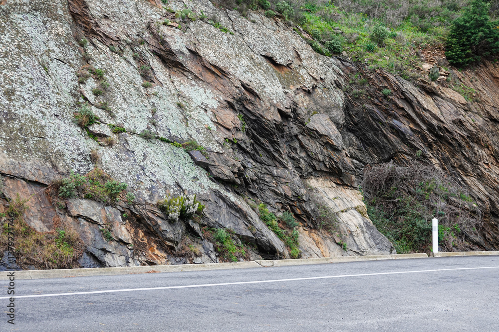 A rocky hillside borders a winding road, showcasing various textures and colors of stone.