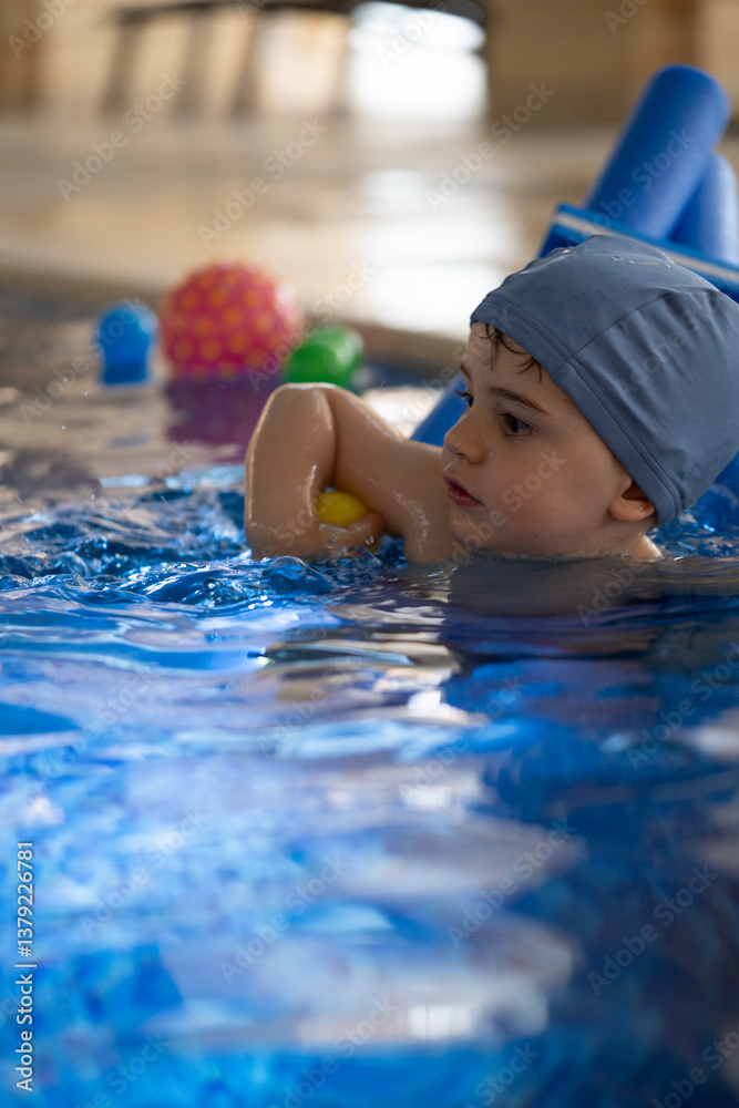 Obraz premium Child swimming with floatation device and balls in pool