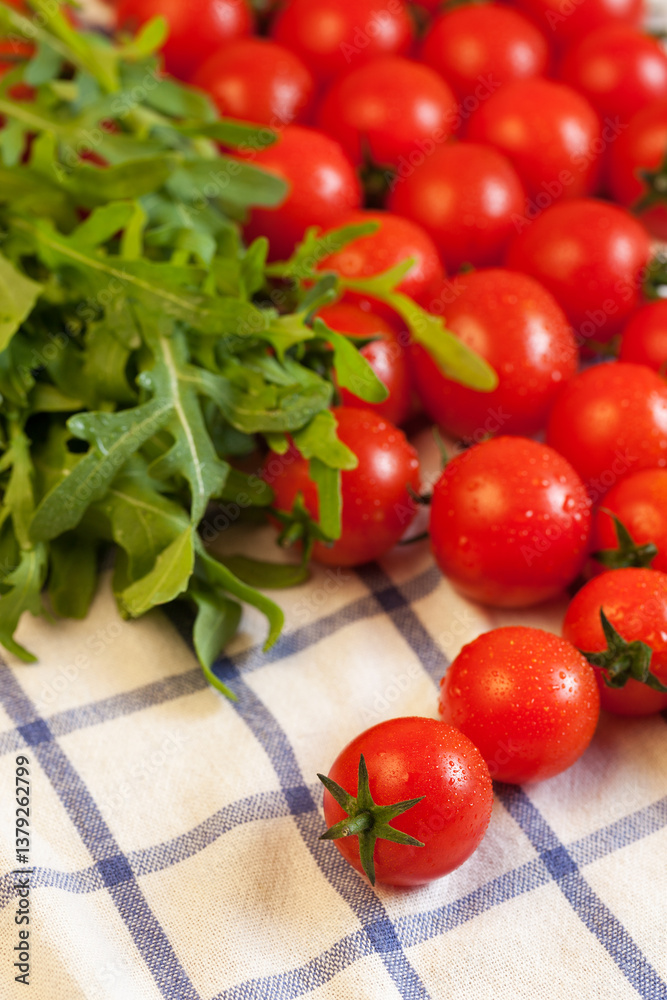Red ripe cherry tomatoes and fresh spicy rocket salad on white checked towel, focus on foreground