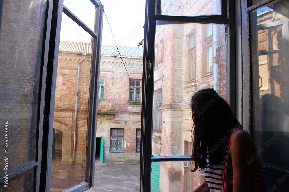 Exploring the tranquility of an old building while gazing out the window in an urban courtyard during daylight hours Exploring the tranquility of an old building while gazing out the window in an urban courtyard during daylight hours