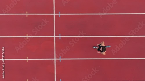 Aerial top view of a solo male athlete sprinting along a marked track lane, showcasing the track boundaries, emphasizing speed, focus, and precision in motion. Cinematic drone slow motion