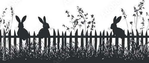 Silhouette of rabbits sitting on a picket fence surrounded by grass and flowers.