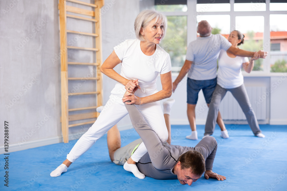 Fototapeta premium Sportive aged lady practicing arm twist technique against her partner during self-defense courses