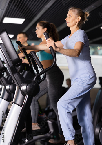Elterly fitness woman in sportswear doing cardio training on ellipsoid in gym