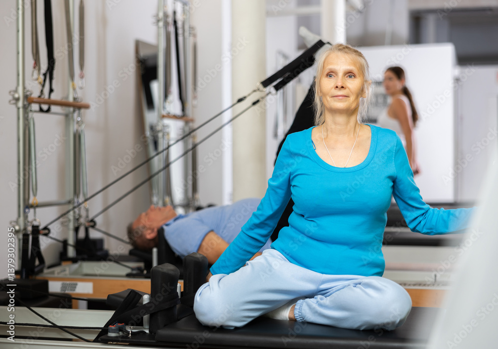 Positive mature female in activewear training twist rotation while using Pilates performer bed in gym Positive mature female in activewear training twist rotation while using Pilates performer bed in gym