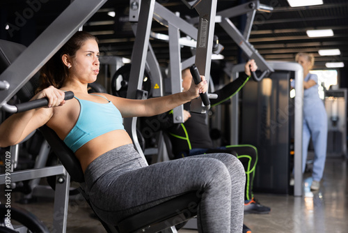 Young woman trains her arm muscles using a simulator in the gym