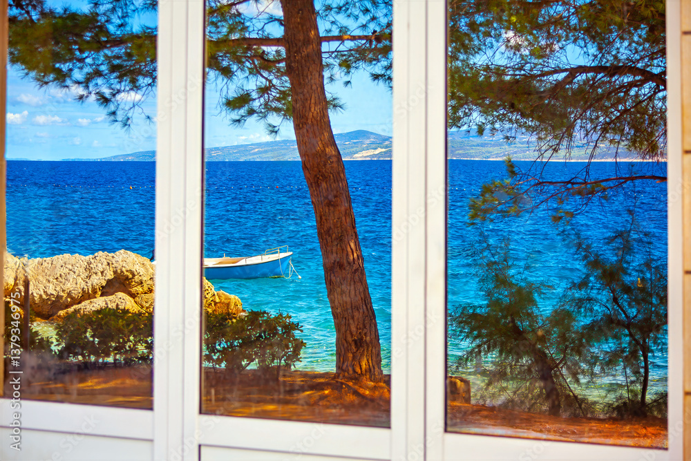 Glass window reflects stunning seaside view with small boat floating on turquoise water, framed by lush greenery and rocky shore. Serene coastal scene captures essence of relaxation and natural beauty