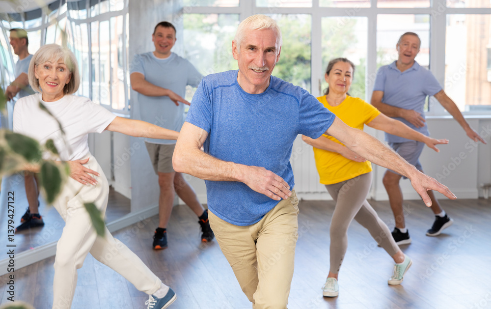 Expressive cheerful gentleman participating in upbeat Zumba class for group of seniors in mirrored fitness studio