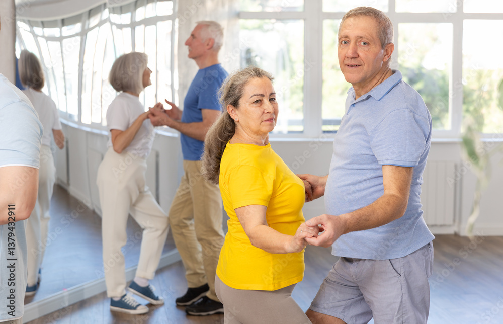 Fototapeta premium Cheerful senior woman practicing passionate samba with interested attentive man in dance class for adults. Amateur dancing concept..