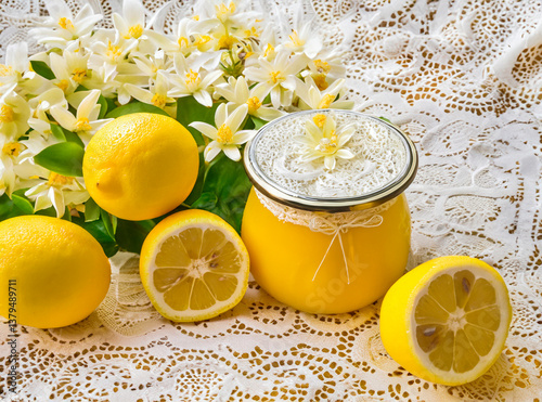 Lemon curd in a jar with lemon flowers and lemons on a lace tablecloth 
