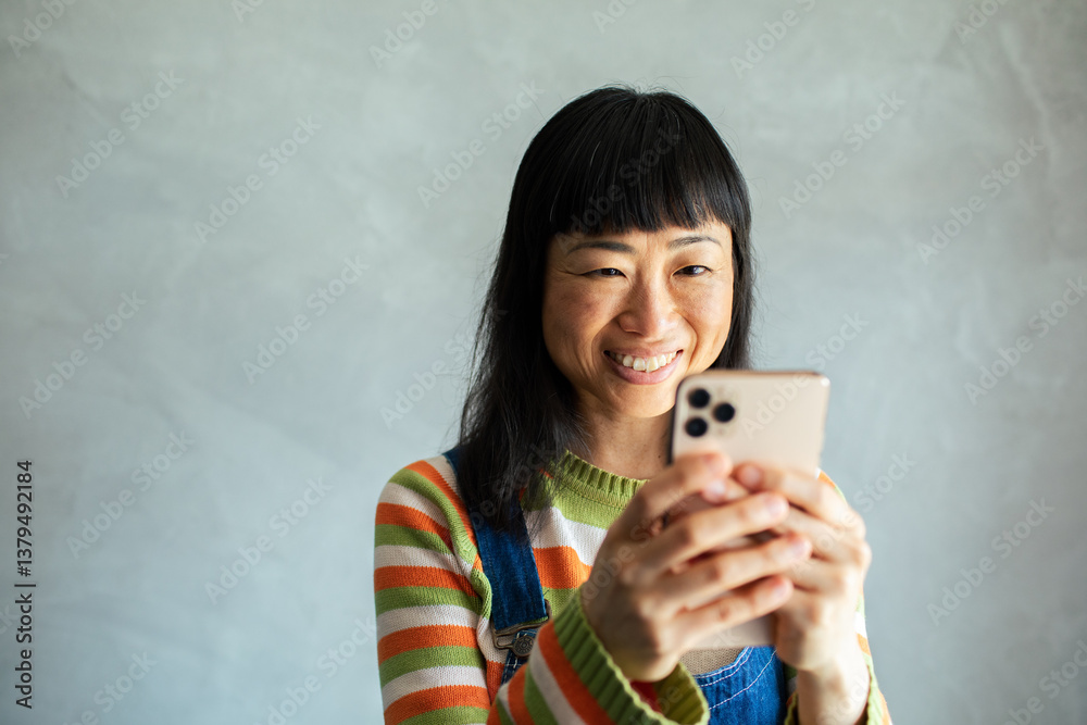 Smiling Asian woman using smartphone on couch at home Smiling Asian woman using smartphone on couch at home
