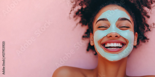 Close-up of a smiling young woman with a face mask on a pink background.