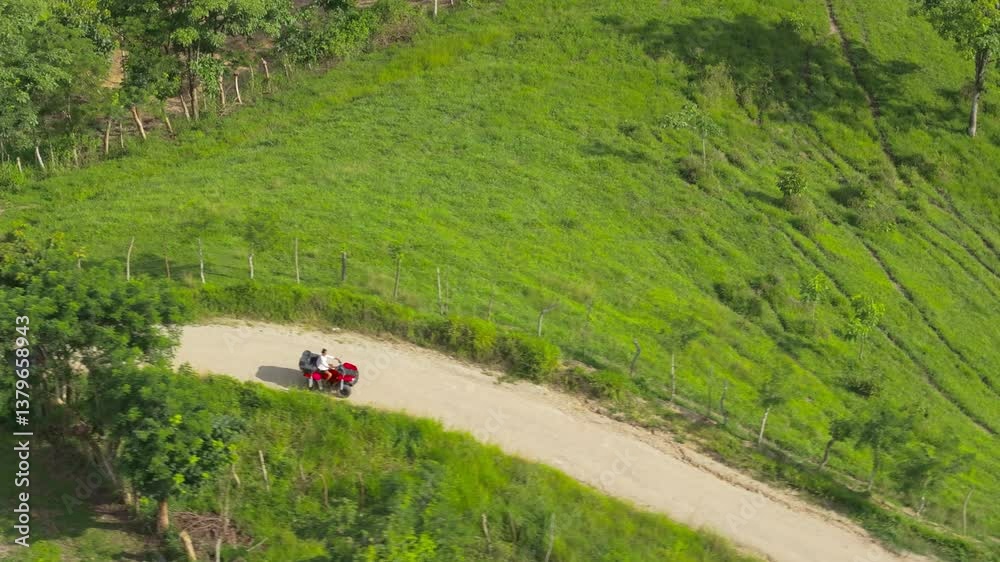 A breathtaking aerial shot shows a young man riding a powerful quad bike on a dirt road surrounded by vibrant green fields in Costa Rica, highlighting the beauty of nature and adventure