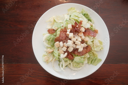 Traditional caesar salad in a white bowl with leaves and a sauce boat and parmesan. Selected focus.