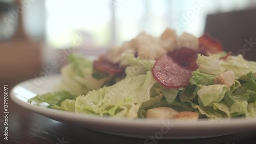 Traditional caesar salad in a white bowl with leaves and a sauce boat and parmesan. Selected focus.