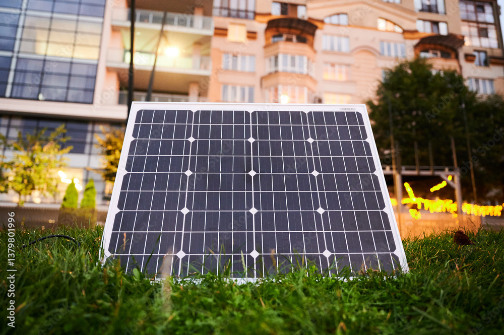 Fototapeta premium Photovoltaic solar panel in front of modern apartment building with balconies, suggesting residential or mixed-use. Concept of integration of sustainable renewable energy sources into architecture.