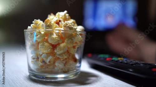 Popcorn in a cup in front of the TV. A hand takes popcorn from a cup.
