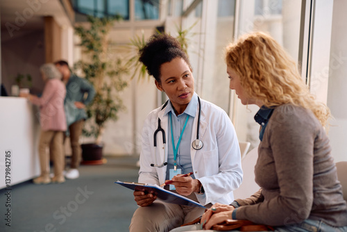 Quadro em tela Black doctor and her female patient going through medical report at clinic