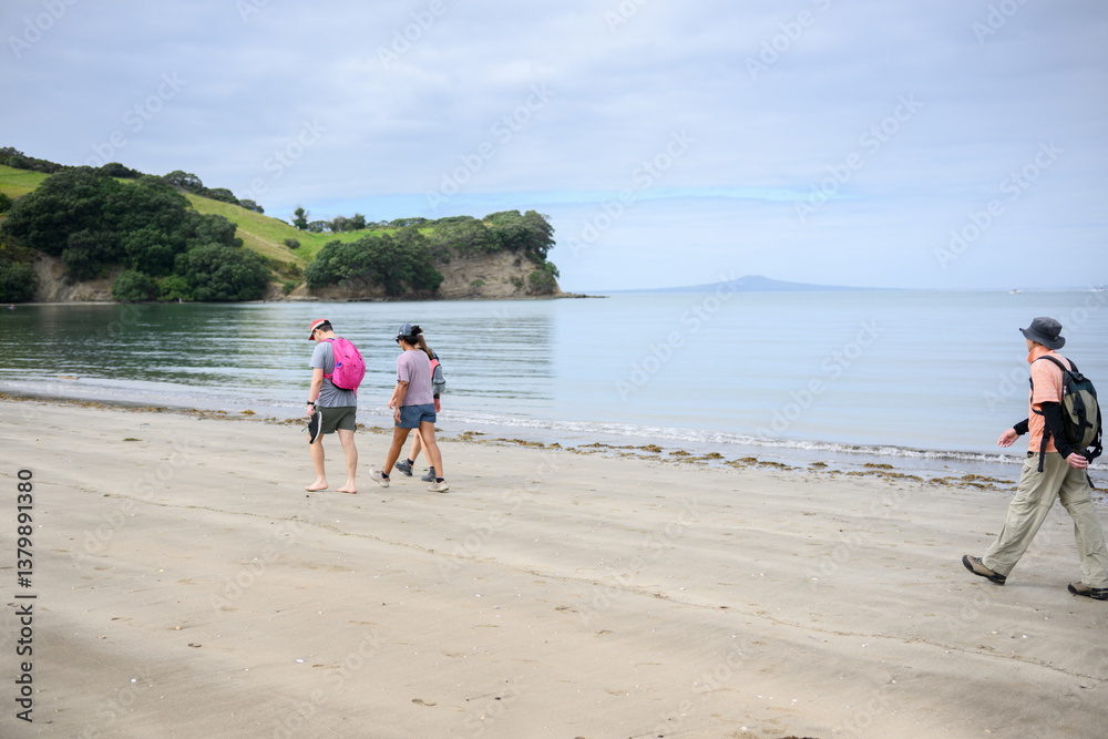 People walking on the beach at Shakespear Regional Park. Rangitoto Island in the distance. Auckland.