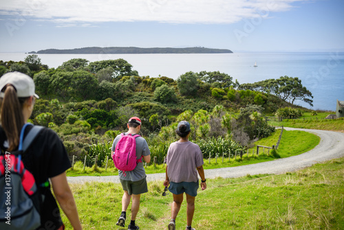 Obraz na płótnie Three people walking on the green hill at Shakespear Regional Park. Auckland. w salonie
