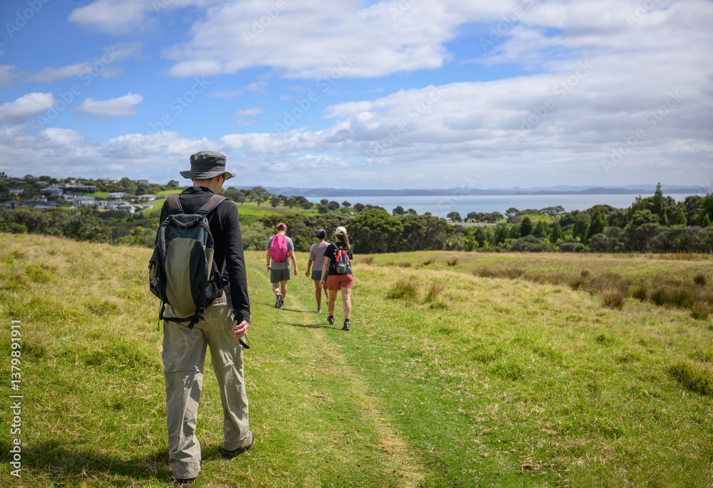 Group of people walking on green hill at Shakespear Regional Park. Auckland.