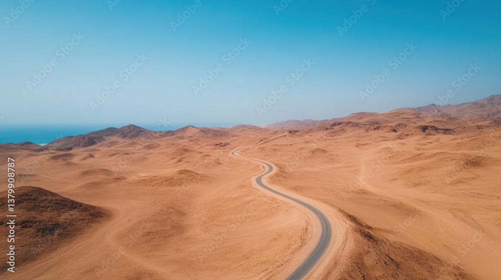 Fototapeta premium Winding desert road stretches through vast sandy landscape under clear blue sky