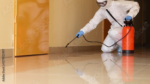 Worker in chemical protective suit sprays insecticide in tiled room. Pest control employee helps to eliminate the cockroach infestation in house