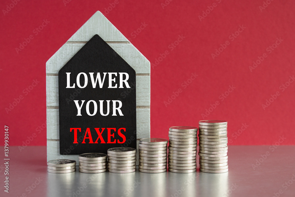 Lower your taxes symbol. Concept words Lower your taxes written on a black board. Silver coins arranged in a graph in front. Beautiful red background, grey table. Business concept.
