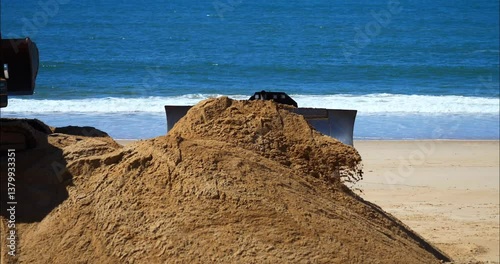 Bulldozer and crane handling sand to combat beach erosion.