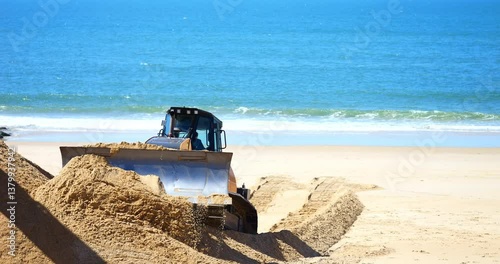 Bulldozer and crane handling sand to combat beach erosion.