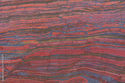 Faceted red stone with natural patterns and texture. Banded iron ore. Mineral structure, geological layers, natural background for design.