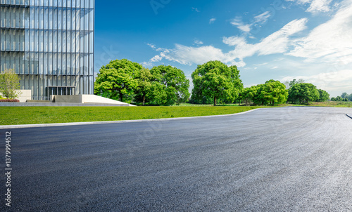 Obraz na płótnie Empty asphalt road curves past a modern glass office building and green park trees under the blue sky w salonie