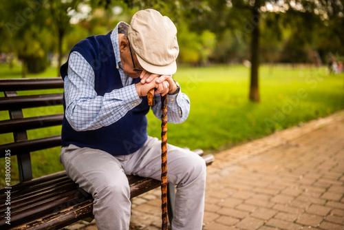 Elderly man sits alone on a wooden bench in the park. He is depressed.