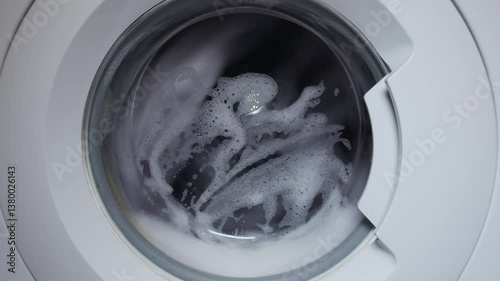 Inside a washing machine, clothes spin in soapy water. Closeup view