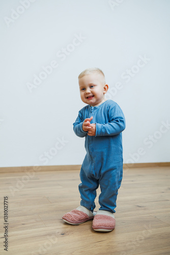 A cheerful and joyful toddler dressed in cozy blue pajamas is happily standing on a wooden floor, radiating a delightful expression that captures pure innocence and fun during playtime
