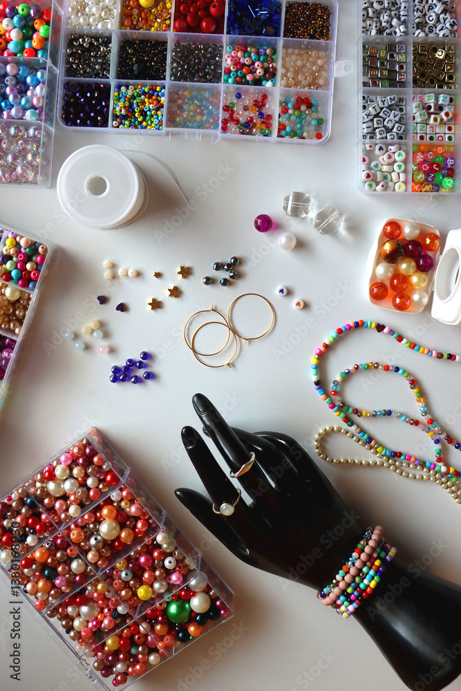 Hand figurine, colorful friendship bracelets, necklaces, various beads and DIY supplies on the table. Making jewelry at home. Flat lay.