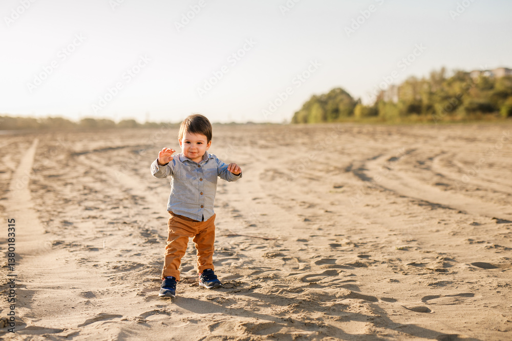 One-year-old boy in a checkered shirt and brown pants taking his first steps on the sand One-year-old boy in a checkered shirt and brown pants taking his first steps on the sand
